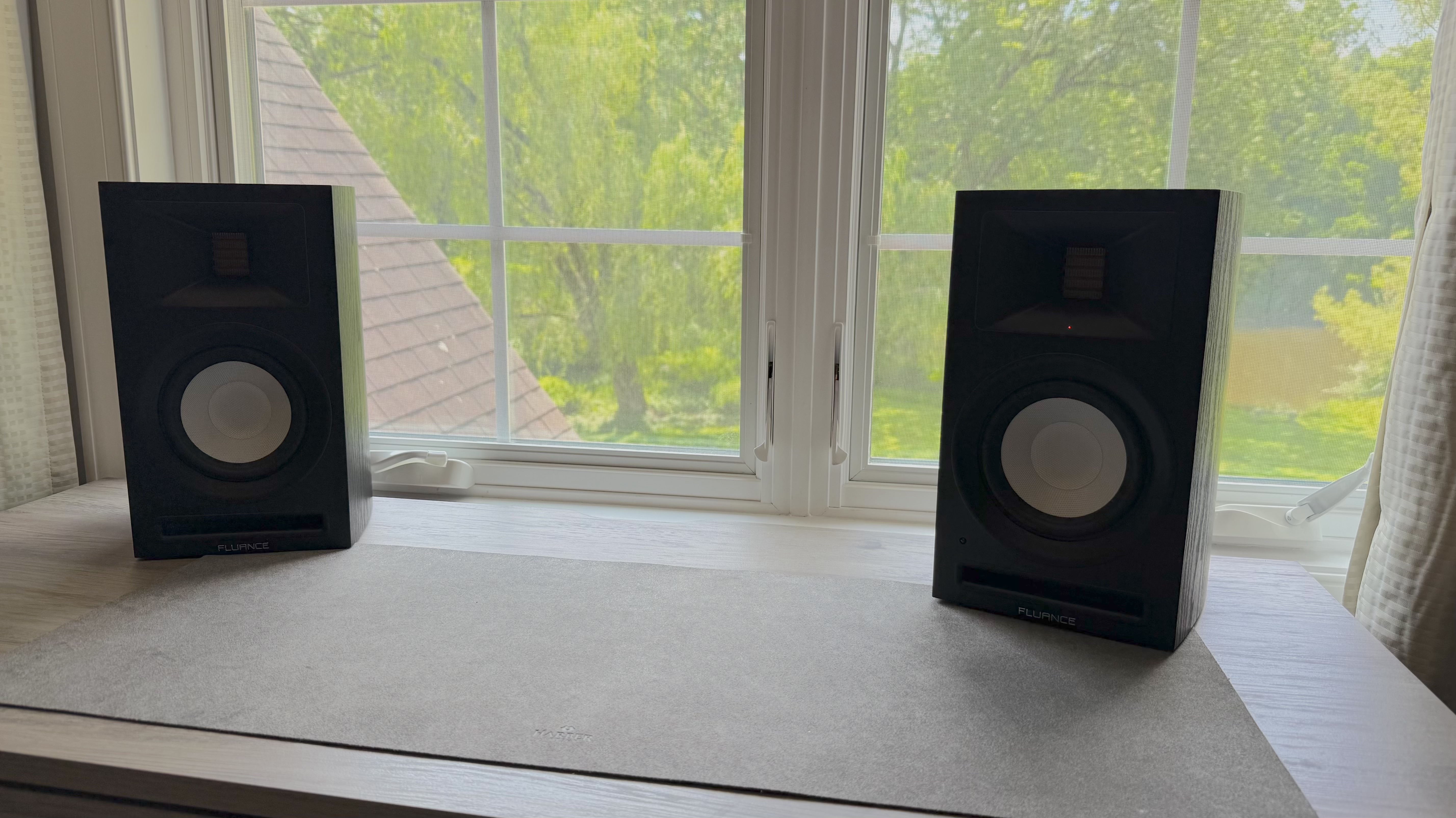 Fluance Ri71 powered bookshelf speakers on a windowsill, with trees outside the window.