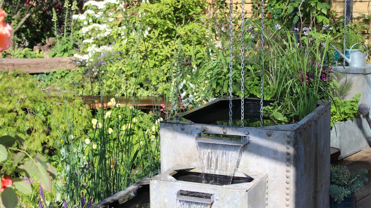 Metal rain pot with rain chains in an established garden