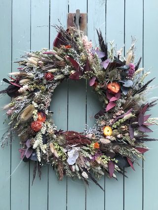 autumn wreath with deep purples and blues and dried flowers on a soft blue background