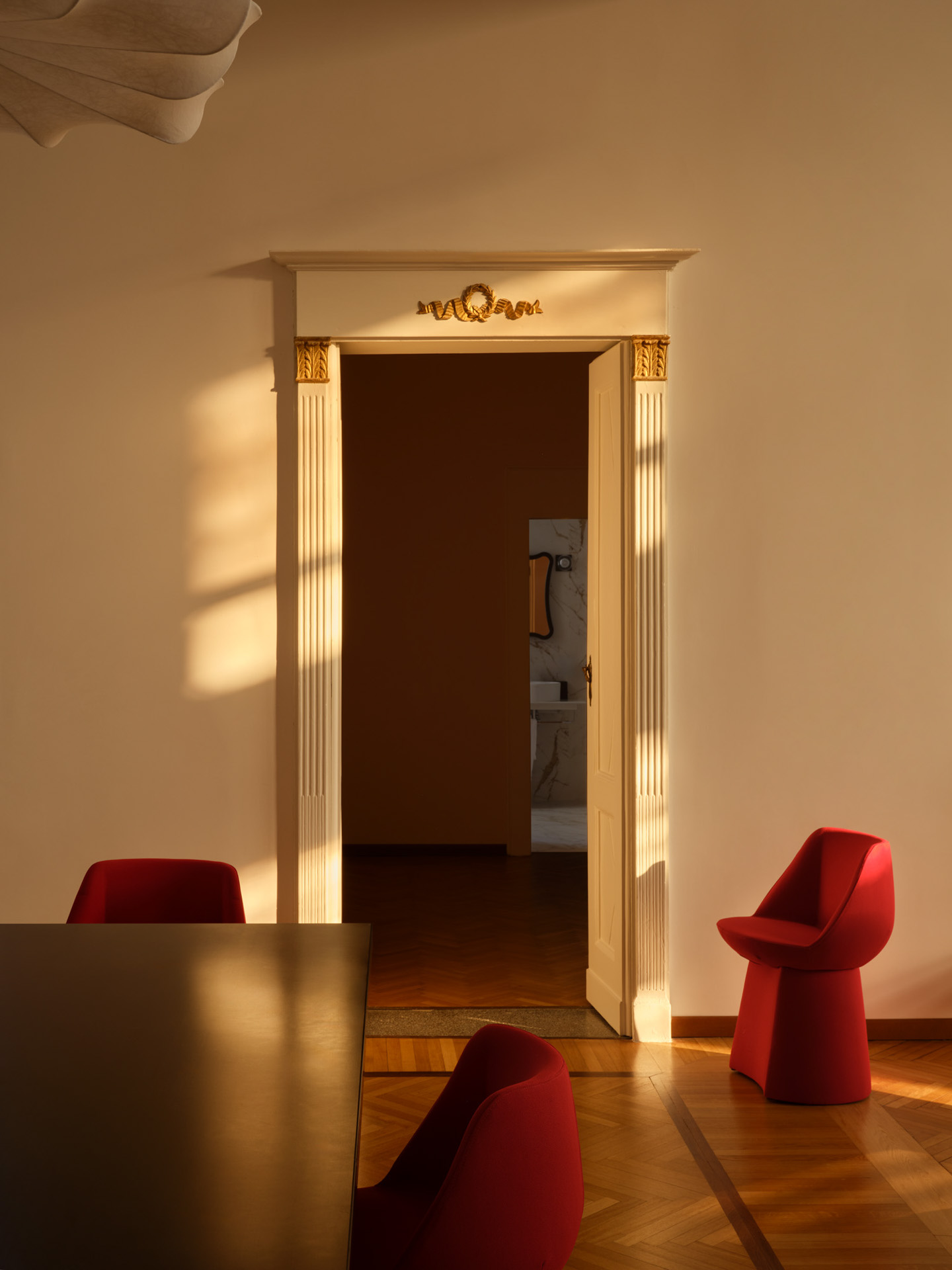 A quirkily decorated hotel suite punctuated by wooden floors and red, chubby chairs in velvet is filled by golden sunshine.