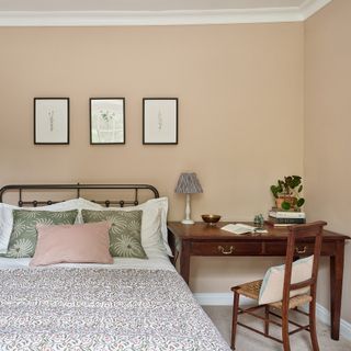 pink painted bedroom with a cast iron bedstead, antique desk and patterned cushions and bed throw