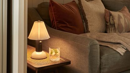A portable table lamp casting a warm glow over a side table next to a fabric couch