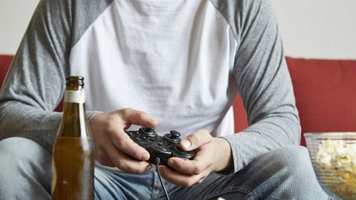 person sitting on a couch playing a video game with a beer bottle on a table