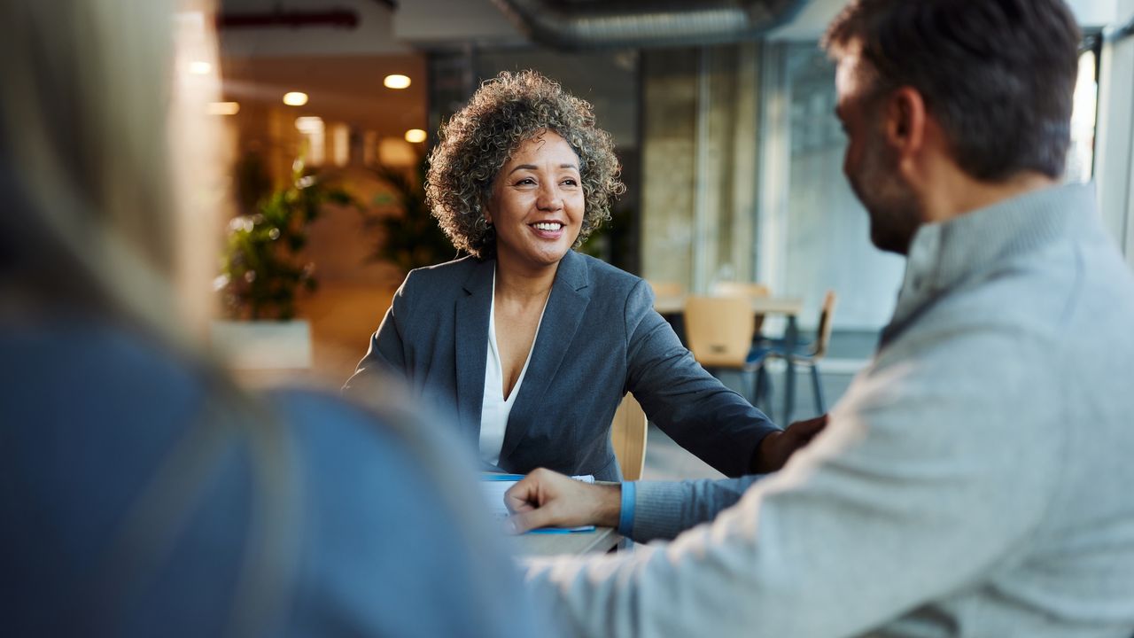 A professional woman talks with a couple at a conference table in an office.