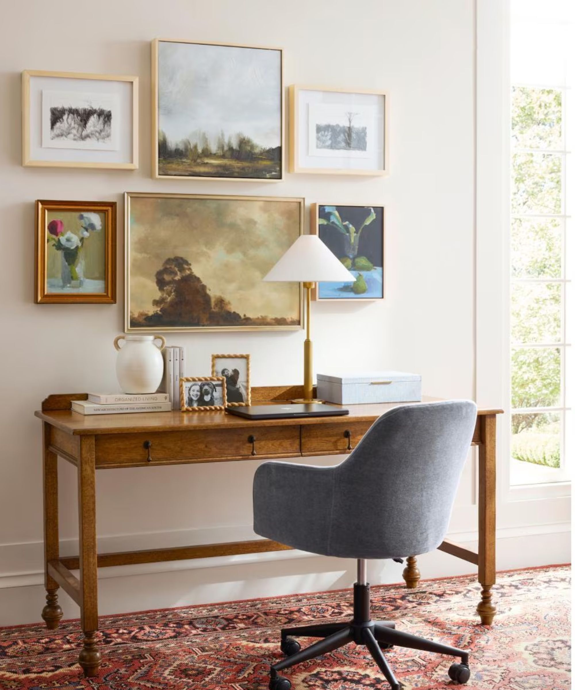 A traditional office space with a grey swivel chair, a wooden desk and a gallery wall of paintings