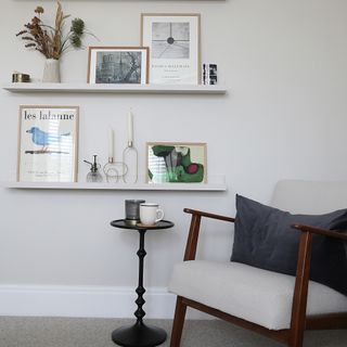 Corner of white bedroom with boucle armchair, side table and floating shelves