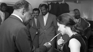 American jazz pianist and composer Count Basie (1904-1984) lights a cigarette in its holder for Princess Margaret, Countess of Snowdon (1930-2002) backstage during the recording of the BBC Television show 'Jazz at the Maltings' at Snape Maltings near Aldeburgh in Suffolk, England on 5th December 1968.