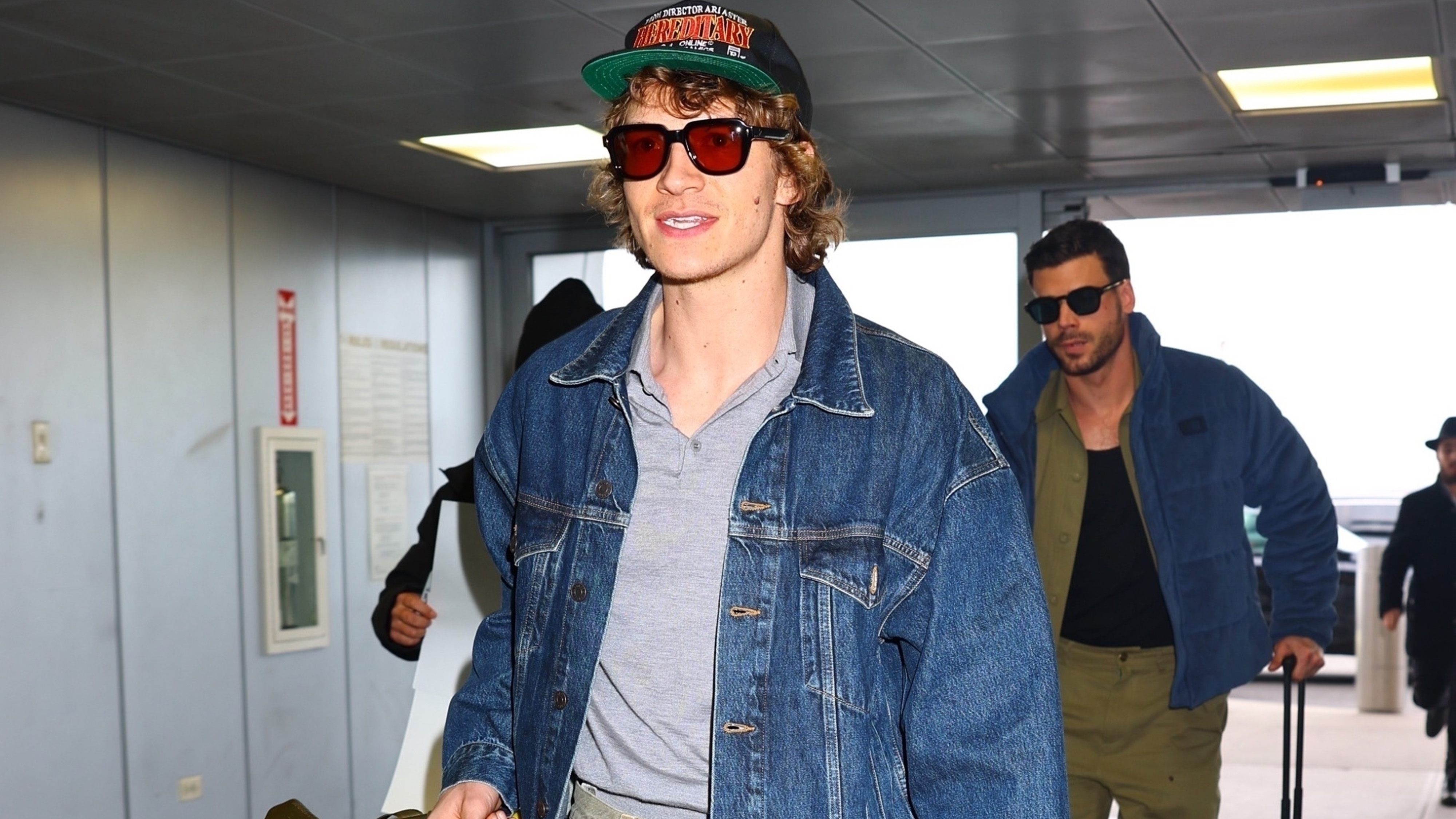 Connor Storrie wears a hat, gray polo shirt, and a denim jacket.