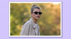 Sofia Richie pictured with her hair up in a bun and wearing a cream coat and black sunglasses/ in a purple template
