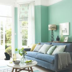 A green-painted living room with a blue velvet sofa and a voile curtain