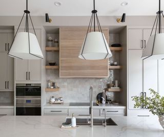 Modern living room with two statement pendants above central marble island, open shelving in the distance with stylishly staged kitchen items and accessories