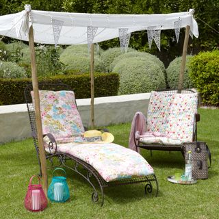 Two metal garden sun loungers with floral cushions arranged under a shade canopy on a grass lawn