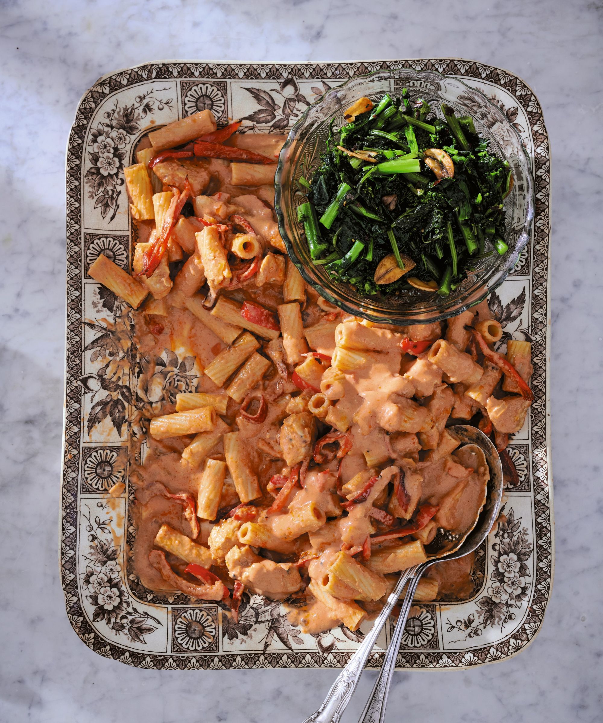 Square bowl filled with pasta and sauce with a small bowl of greens