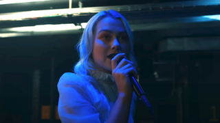 Phoebe Bridgers performing "I Know The End" on Late Night with Seth Meyers in 2020, holding a microphone with blue light on her face