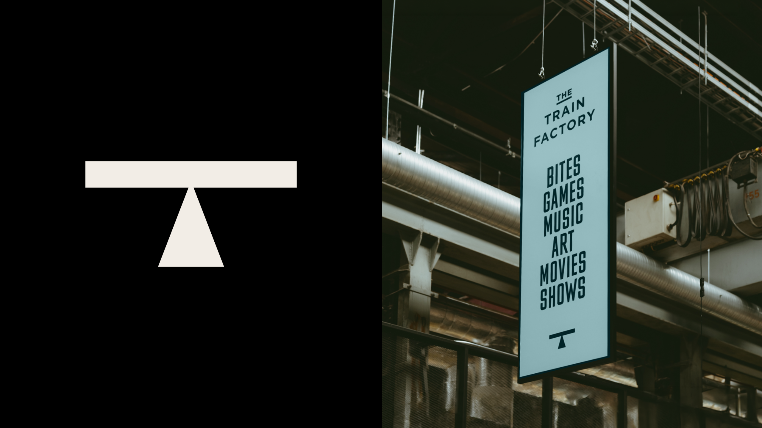 The white "T" logo mark on a black background beside a photo of a pale blue hanging sign reading "The Train Factory, Bites Games Music Art Movies Shows" suspended from ductwork in an industrial space.