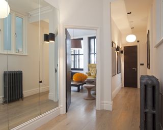 Narrow hallway with oak floor, mirrored panelling, vintage style radiator and artwork on white walls