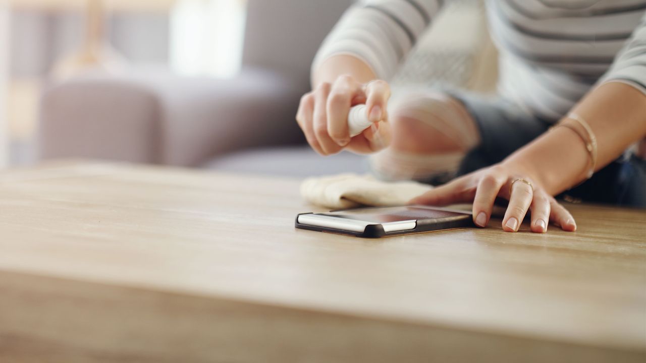 how to clean your phone screen: woman spraying phone with cleaner