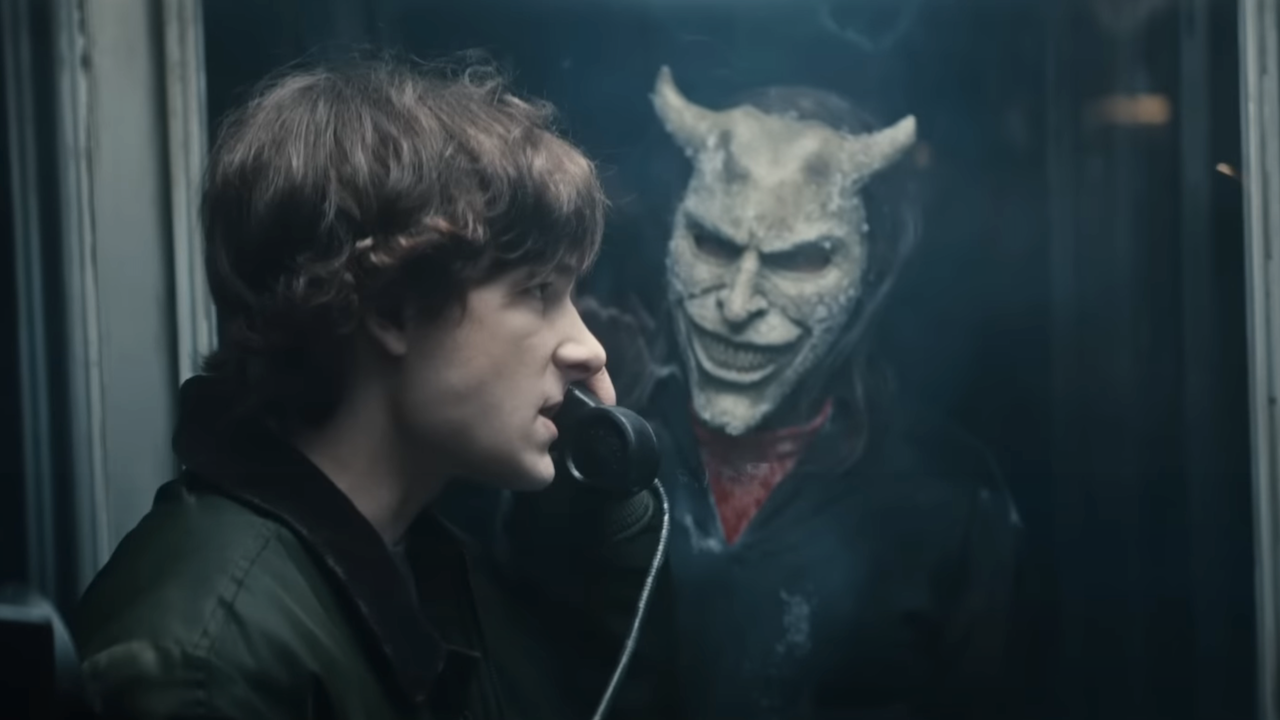 Mason Thames in a phone booth talking into receiver with The Grabber outside the glass in Black Phone 2
