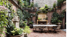 an urban courtyard with various potted plants, brick walls and an antique style table and chairs