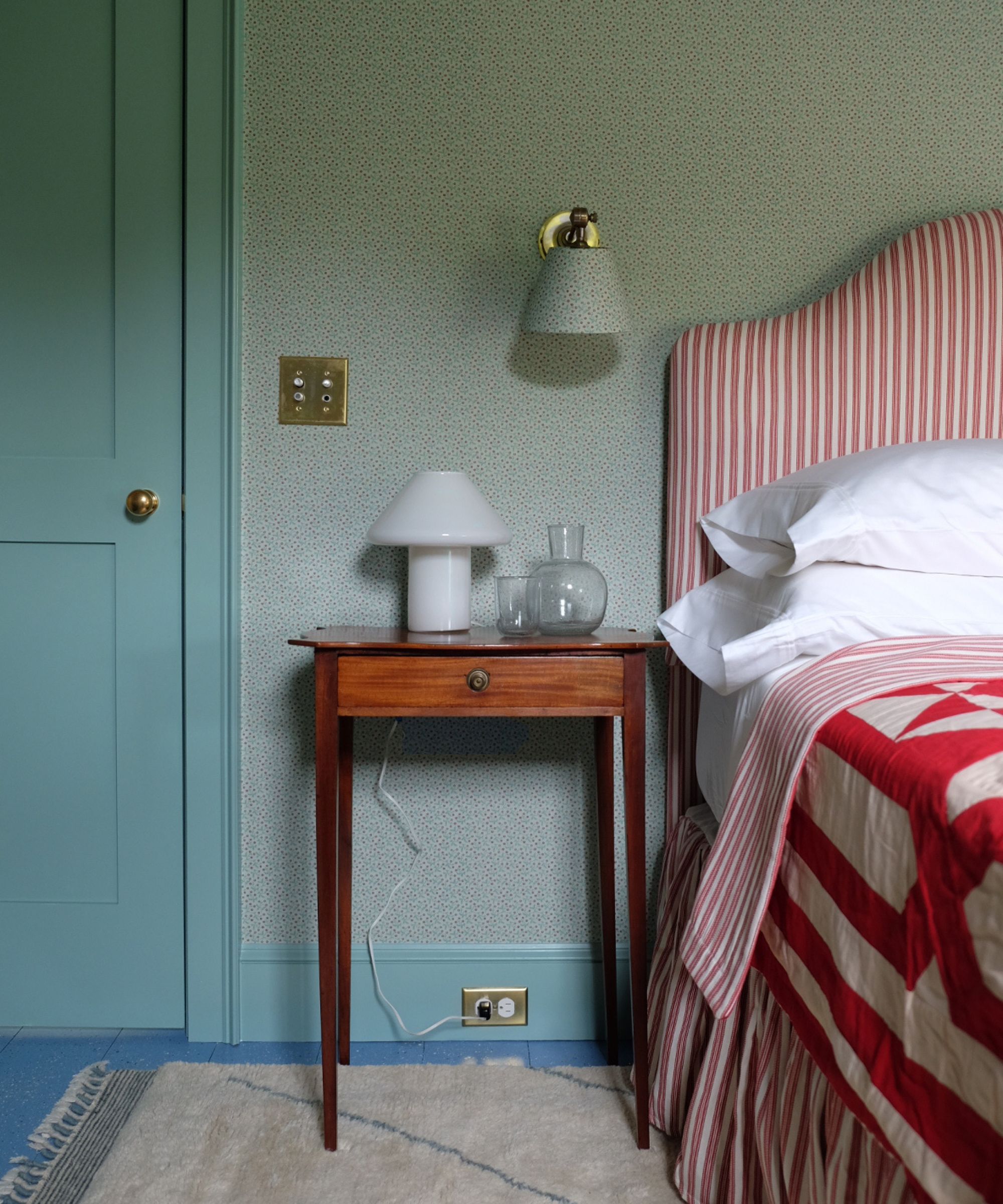 a light blue bedroom with ditsy wallpaper, blue painted door trim and floor and a red stripe upholstered bed