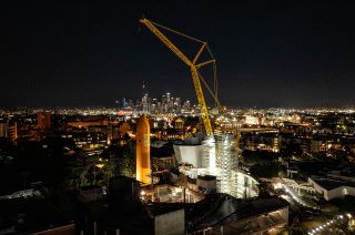 nighttime view of a yellow crane hoisting a vertically oriented, large orange fuel tank.