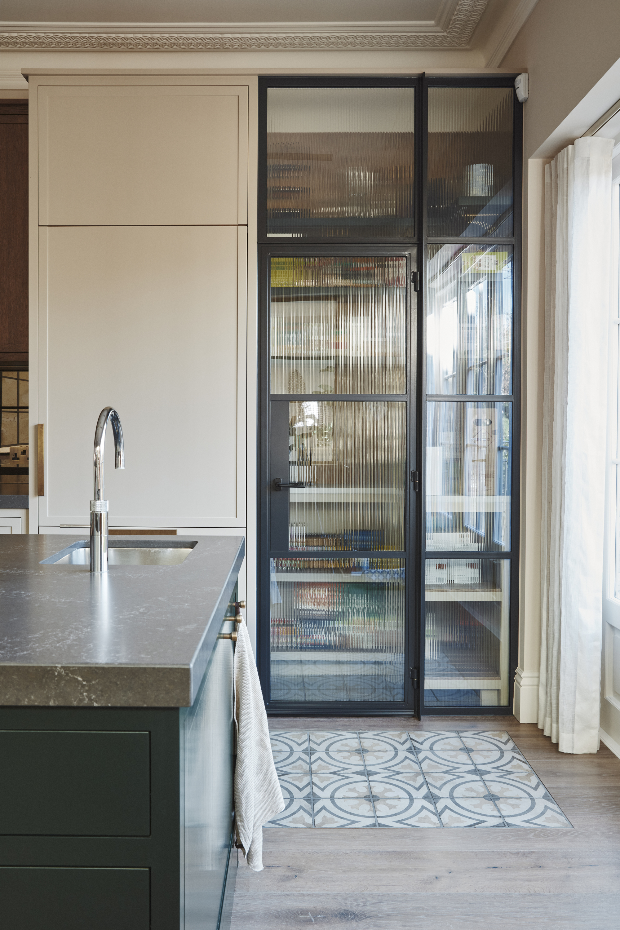 A kitchen with a large glass fronted cabinet and tiled flooring "cut outs" surrounding by wooden floorboards