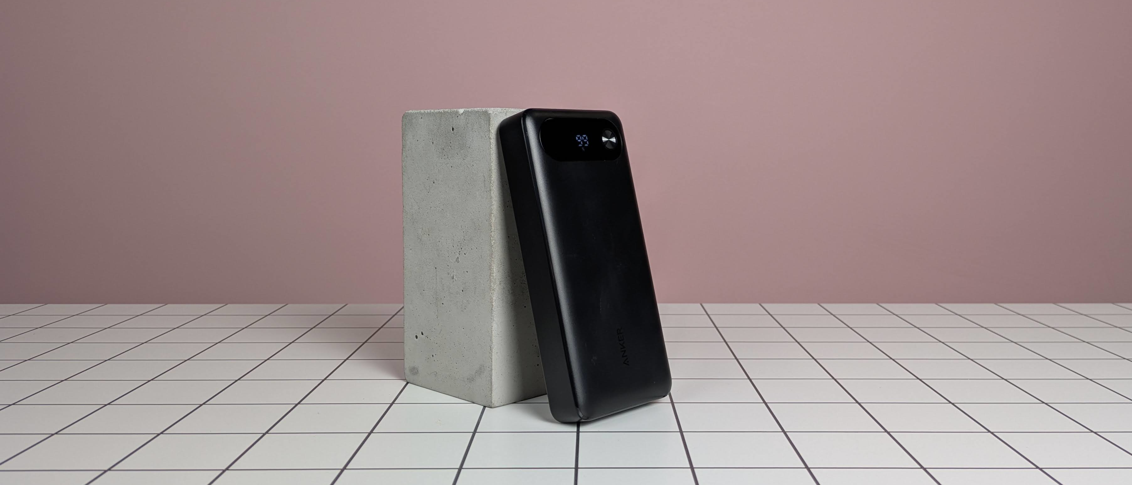 Anker 20,000mAh 87W Power Bank leaning on plinth on desk, with pink background
