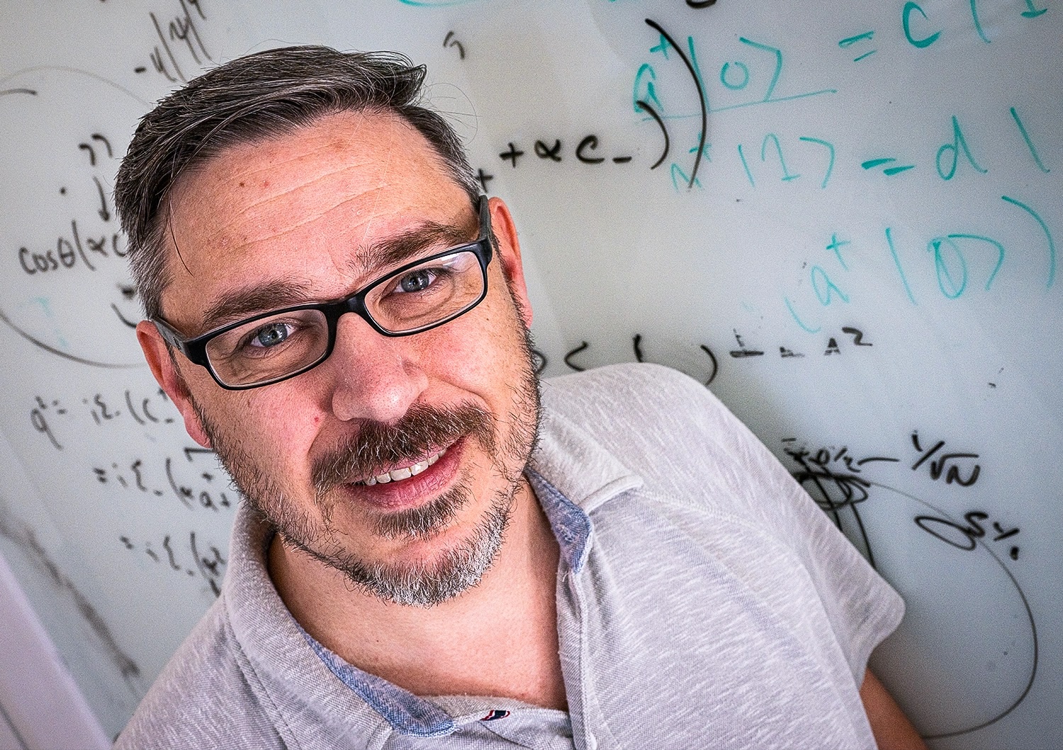 a photo of Kaden Hazzard with a whiteboard full of equations behind him
