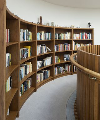 Narrow curved landing with built in bookshelves on one side, grey carpet and wooden balustrade and handrail