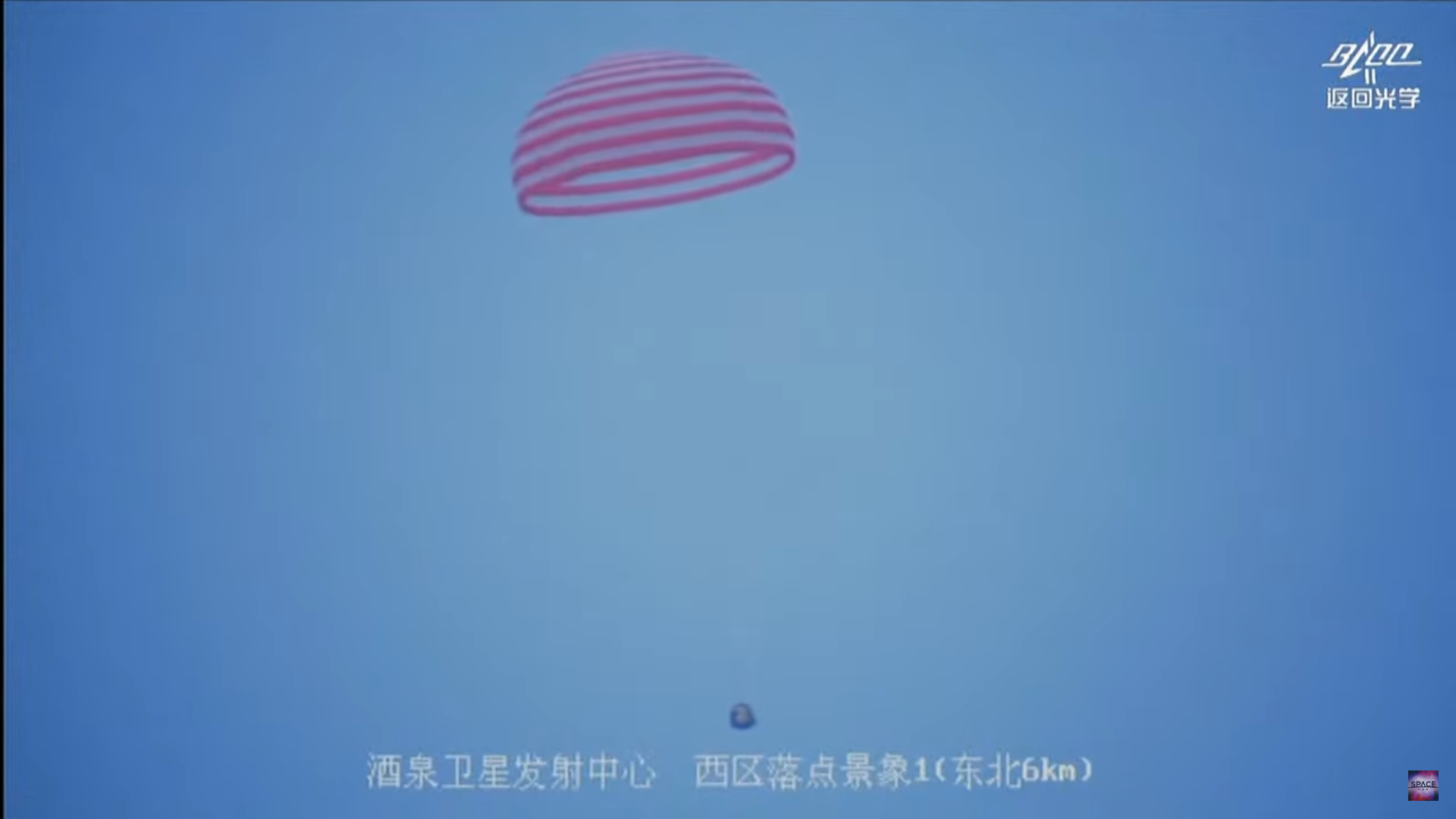 A Chinese space capsule hanging from a parachute as it floats with a blue sky behind.