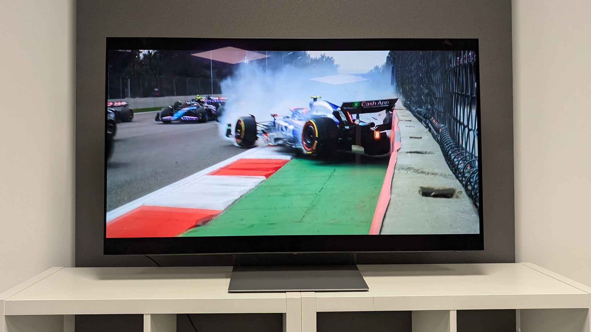 Samsung S90F 48-inch OLED TV on white wooden furniture, on screen are F1 cars