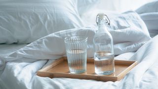 A glass and a bottle of water on a bed