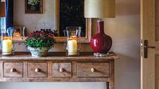 Country-style wood sideboard with red lamp, candle in a glass vase, bowl of red flowers in a marble pot and a mirror 