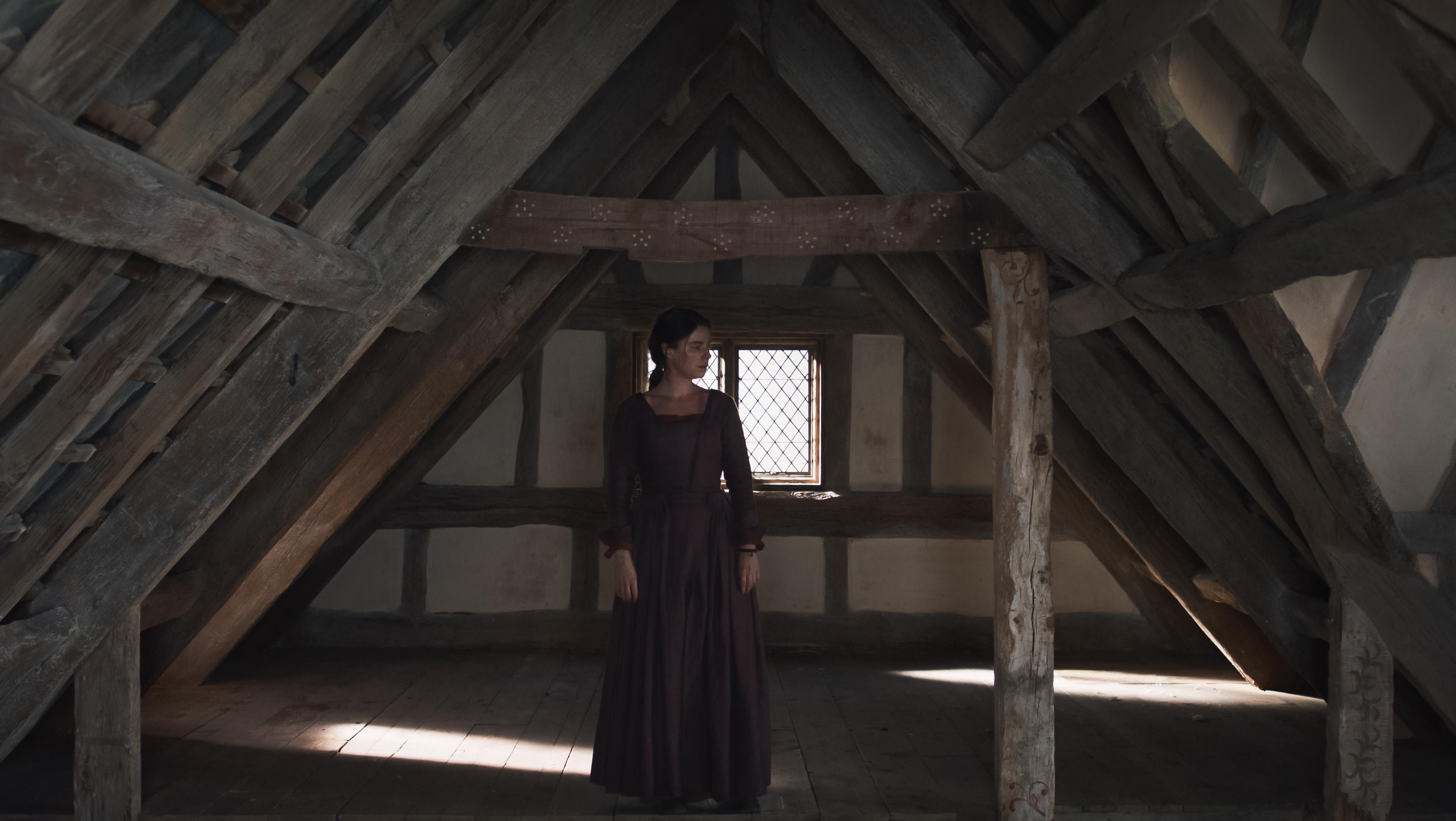 jessie buckley as agnes standing alone in the center of an empty attic in hamnet