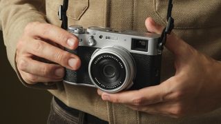 Fujifilm X100VI camera held in two hands against a beige jacket