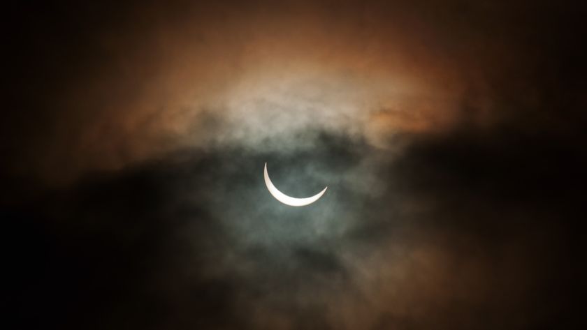 partially eclipses sun appears as a thin crescent behind clouds.