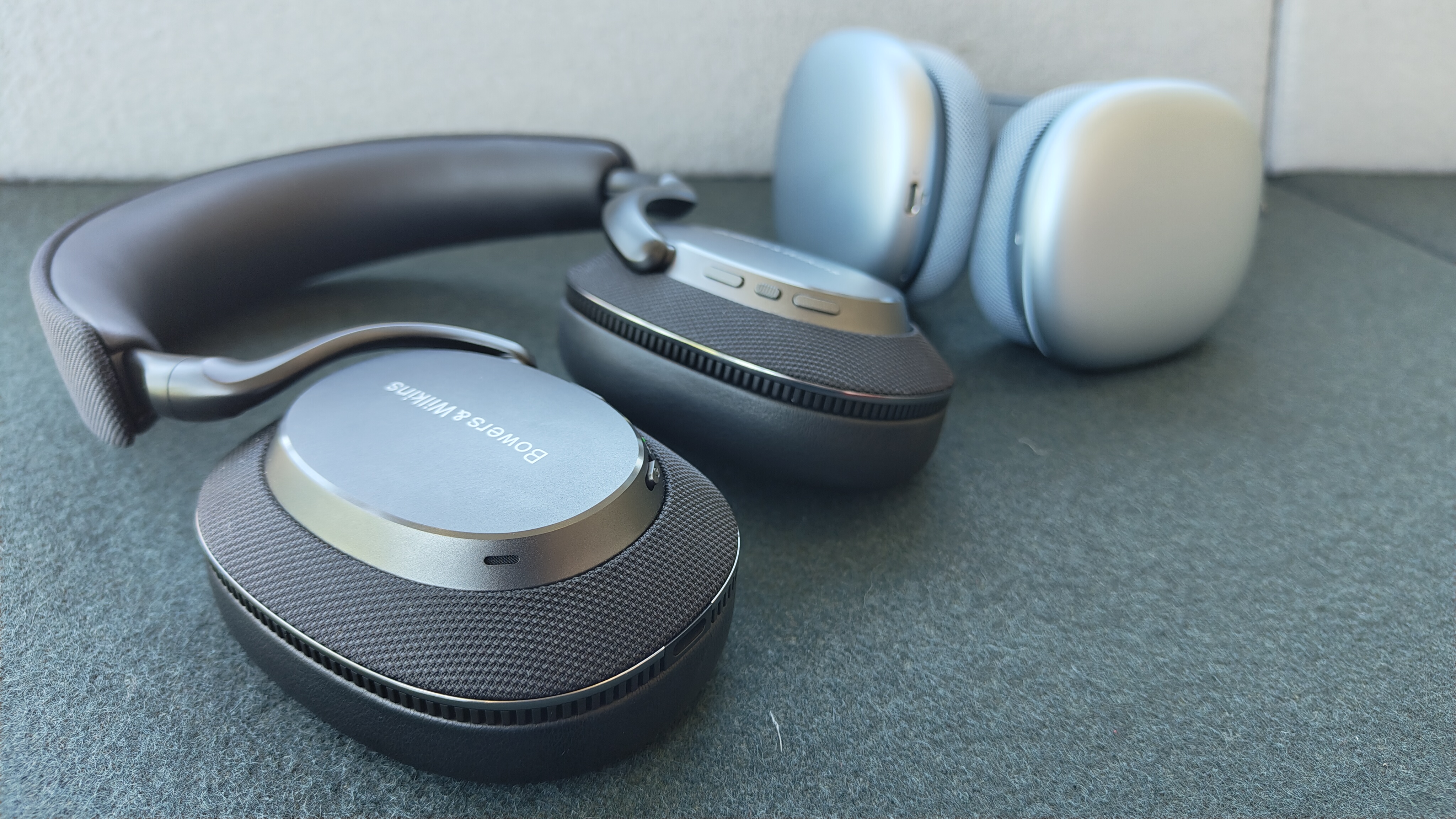 A black pair of B&W Px7 S3 headphones with a blue pair of Apple AirPods Max in the background.