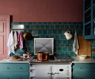 An AGA and blue teal wall tiles and cabinets with a brass rail to hang towels and hanging pots