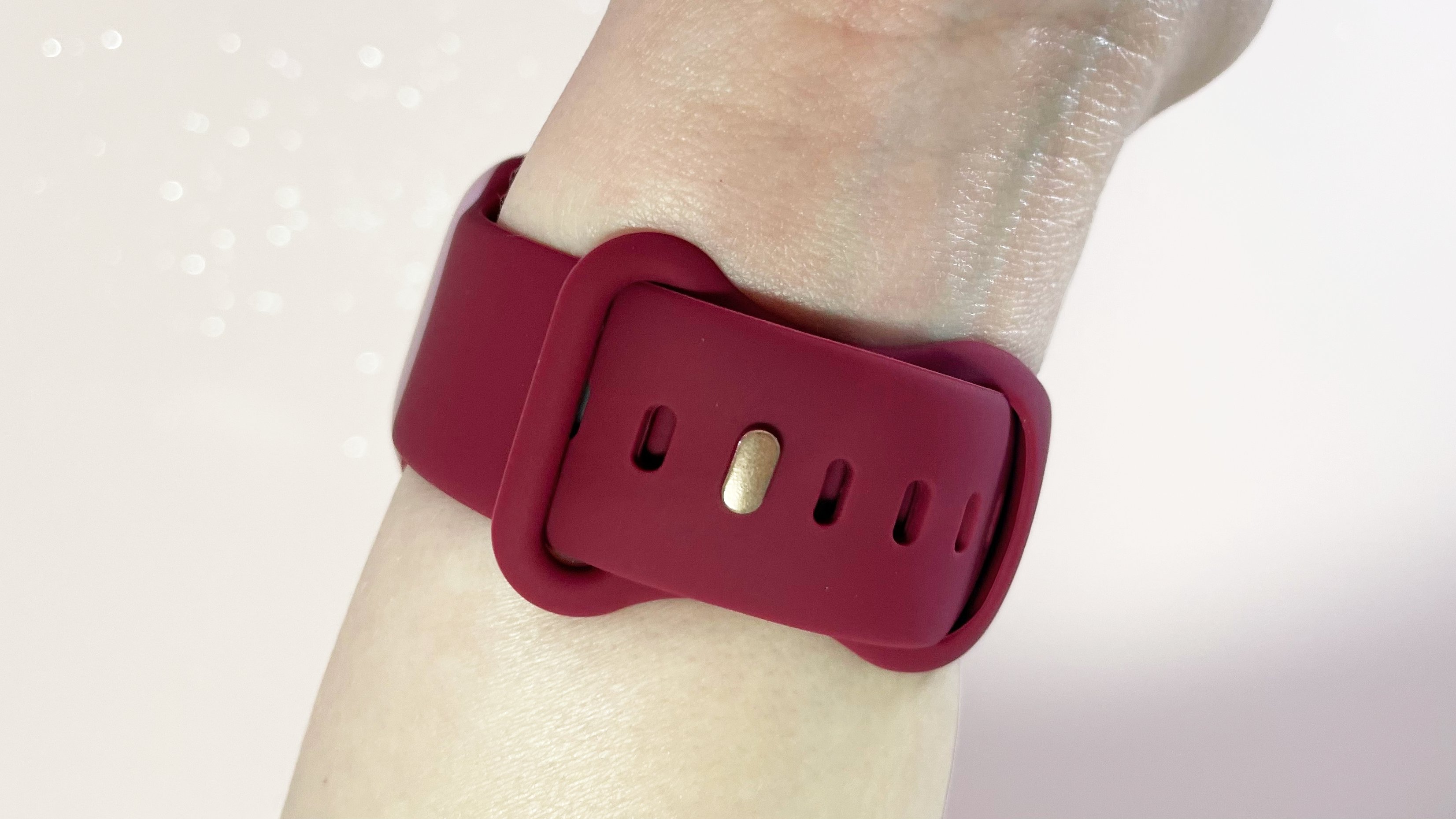 A red silicone Apple Watch-compatible strap is worn on a woman's wrist. The strap and gold-coloured fastening post is in the center of the image.