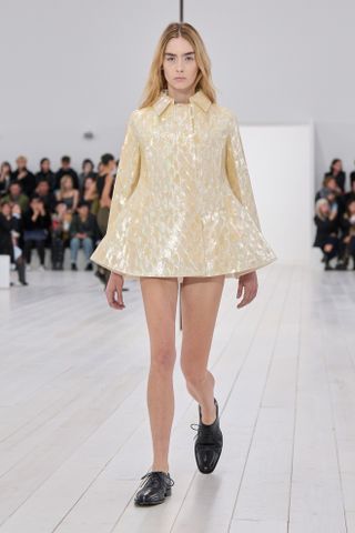 A model at Loewe on the runway during the spring/summer 2025 season wearing a mother-of-pearl minidress with oxford shoes.