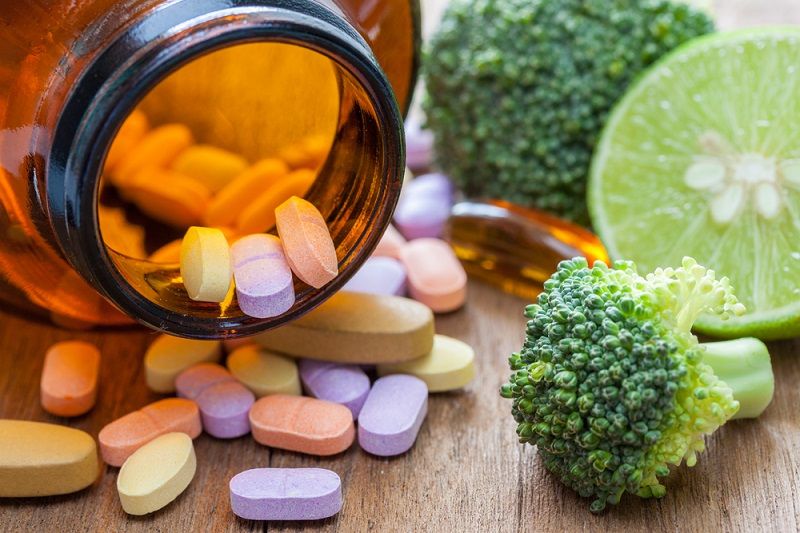 A bottle of supplements next to fruits and vegetables.