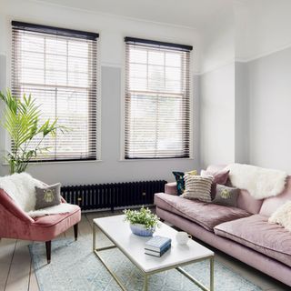 grey and white living room with blind-covered windows and pink colored sofas with a white marble coffee table