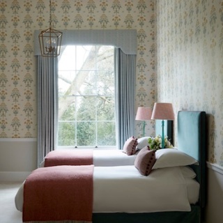 a smart bedroom with twin beds and patterned wallpaper and full height curtains over window