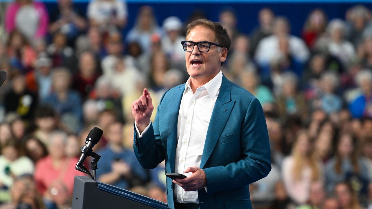 Mark Cuban at a podium in a white buttondown shirt and a teal blazer, giving a speech