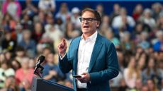 Mark Cuban at a podium in a white buttondown shirt and a teal blazer, giving a speech