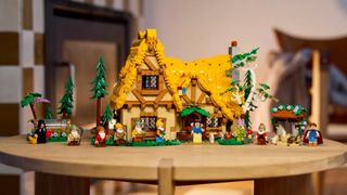 A Lego cottage and minifigures from Snow White and the Seven Dwarfs on a wooden table