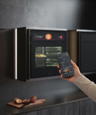 hand holding mobile phone showing app with black oven in background