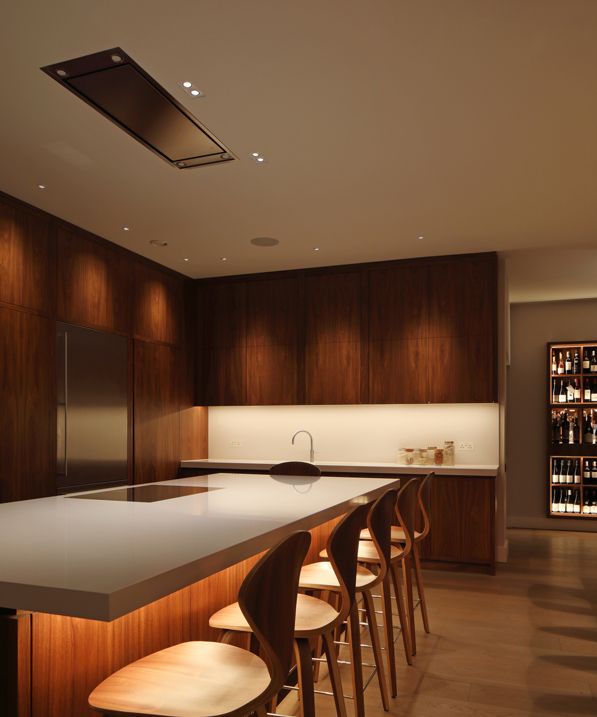kitchen with walnut cabinets, kitchen island with white worktop and recessed lighting below island and cabinets
