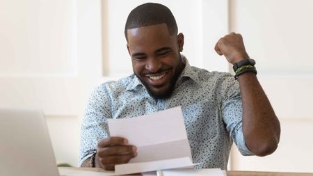 Photo of smiling man looking at papers and pumping his fist