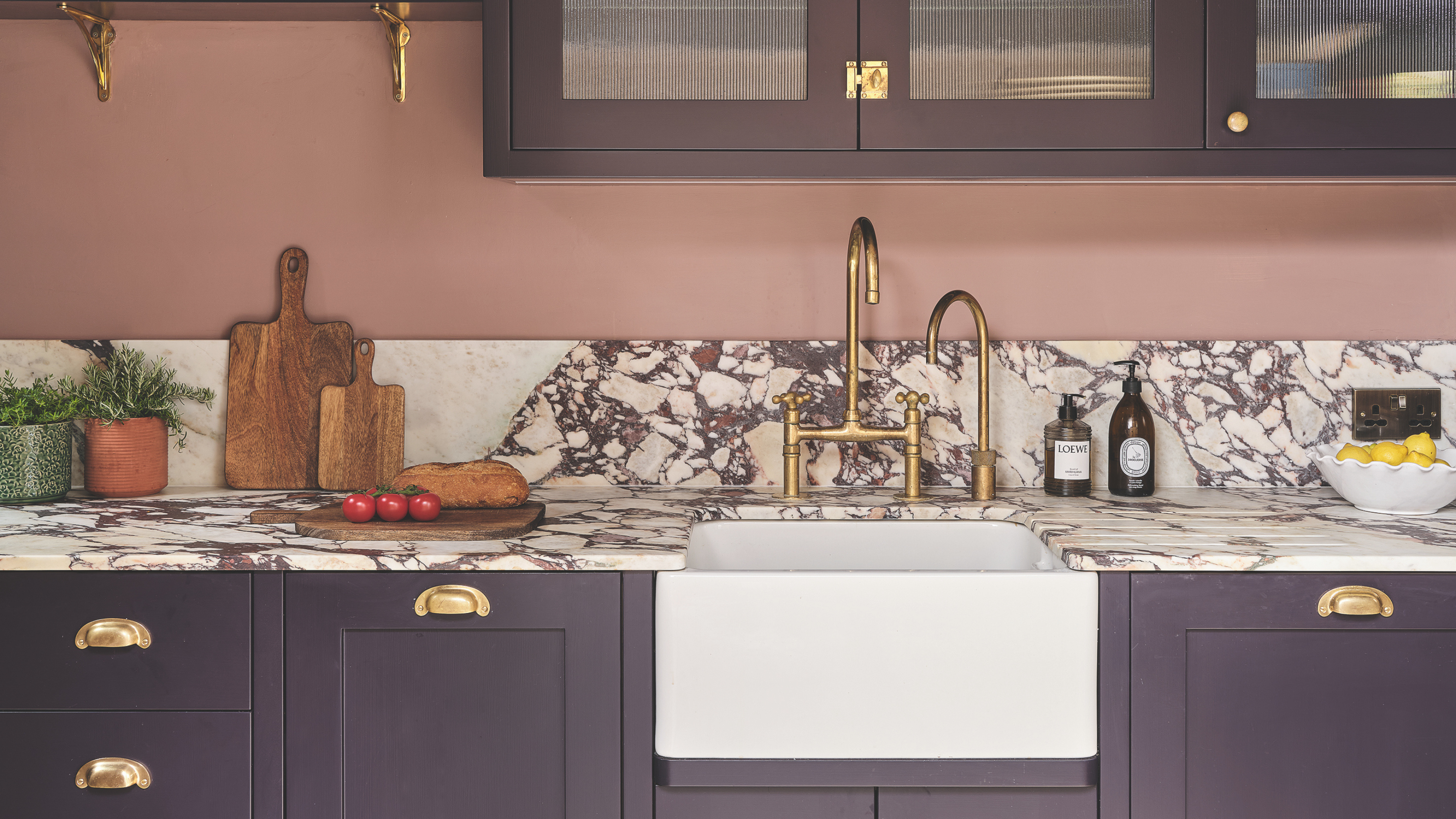 White Belfast sink with gold hardware in a purple and pink kitchen.
